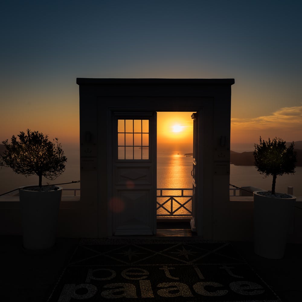 façade wall with window and open door silhouetted against sunset over the ocean