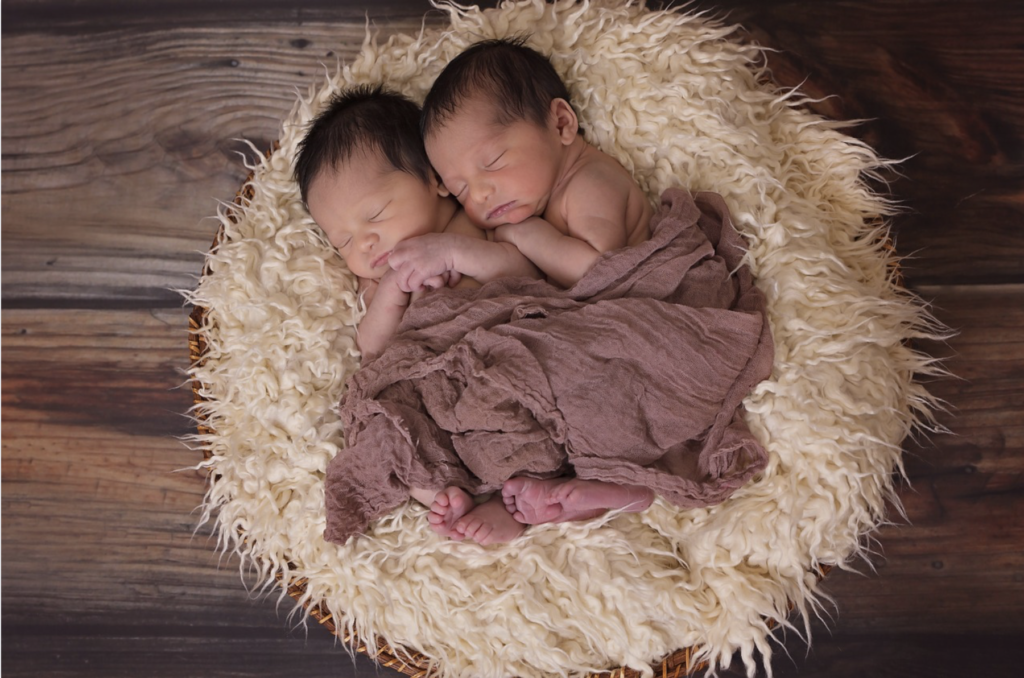 two sleeping babies cuddling together on a rug on a wooden floor (birds-eye view)