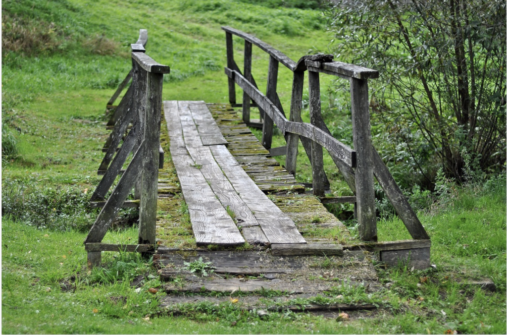 weathered wooden walk way (foot bridge) over green grassy glen creek
