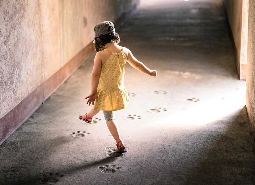 girl in sand-covered hallway stepping in animal footprints
